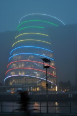 A cyclist whizzes by... the multi coloured Convention Center in the mist...